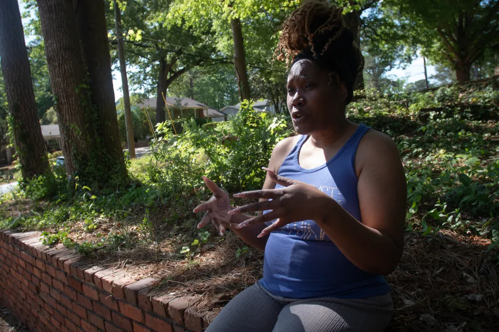 Lakisha Mckinzie, dressed in a blue tank top and dark pants, sits on a brick wall, gesturing with her hands while discussing her ex-housemate.