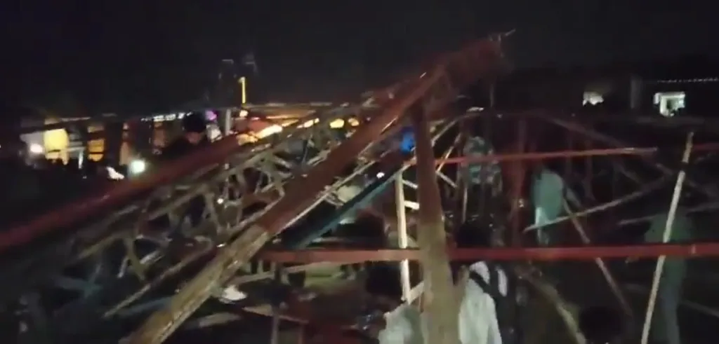 Debris from a collapsed Ferris wheel at night with people trying to help those injured.