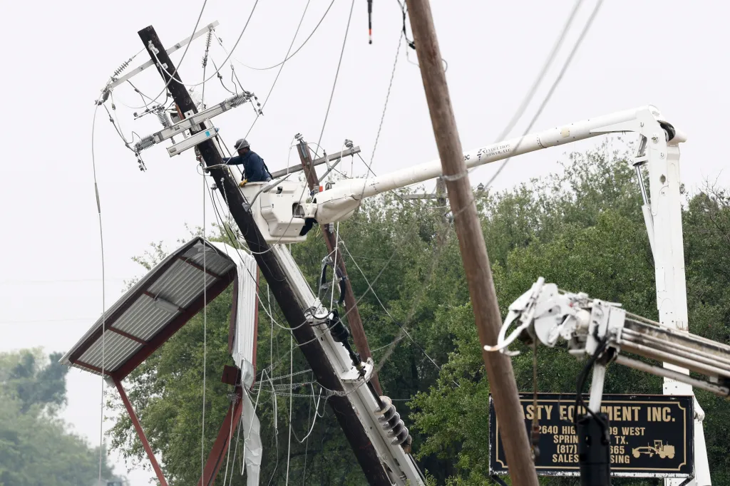 A lineman repairing a damaged power pole from inside a cherry picker bucket, with broken power lines visible against a light sky.
