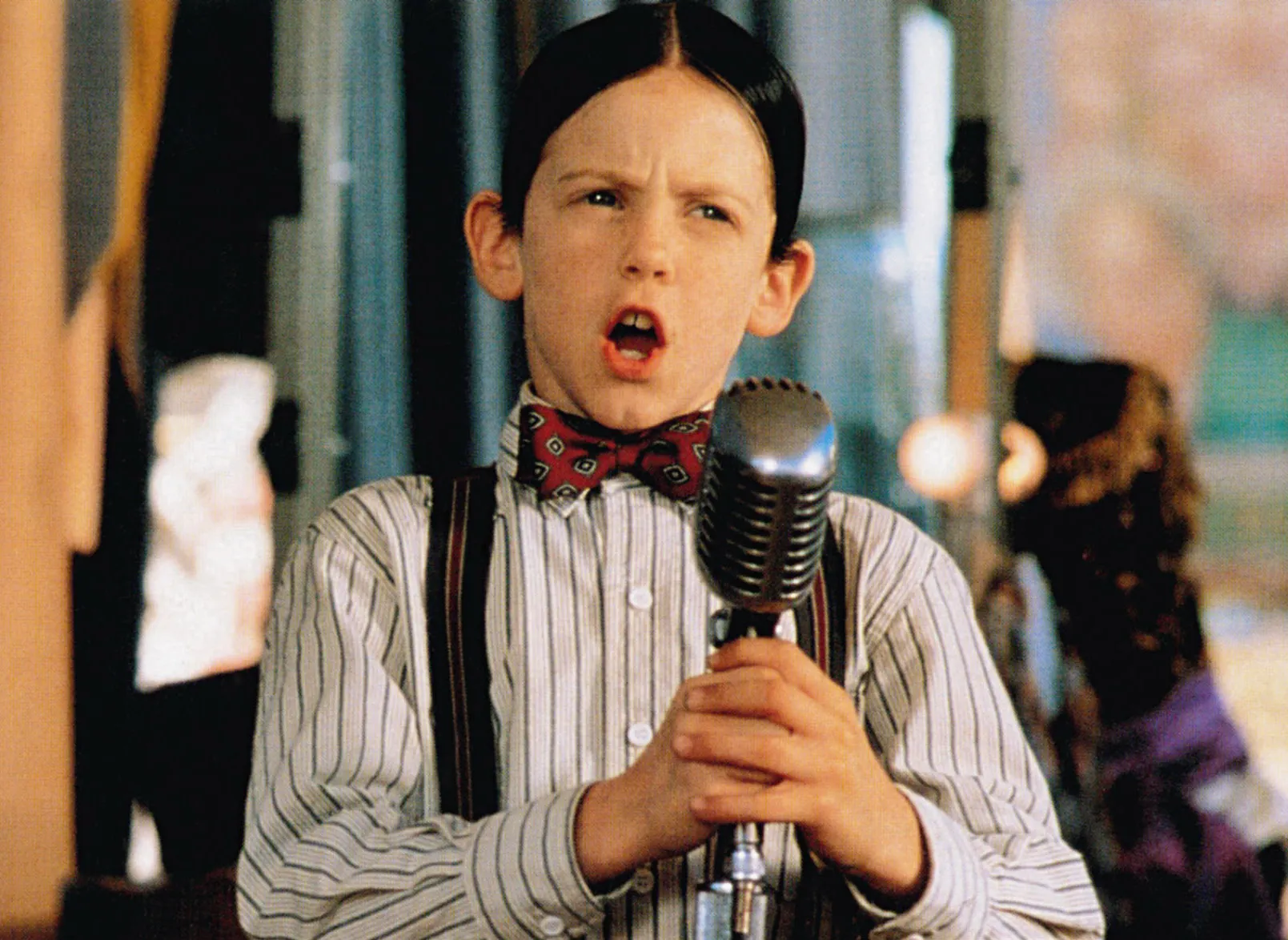 Bug Hall as Alfalfa, wearing a bowtie and suspenders, singing into a microphone in