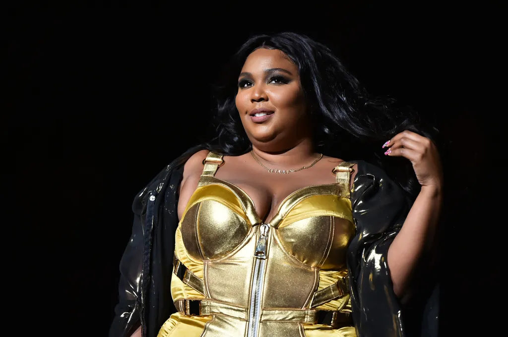 Lizzo on stage wearing a gold bodysuit with a black shiny jacket.
