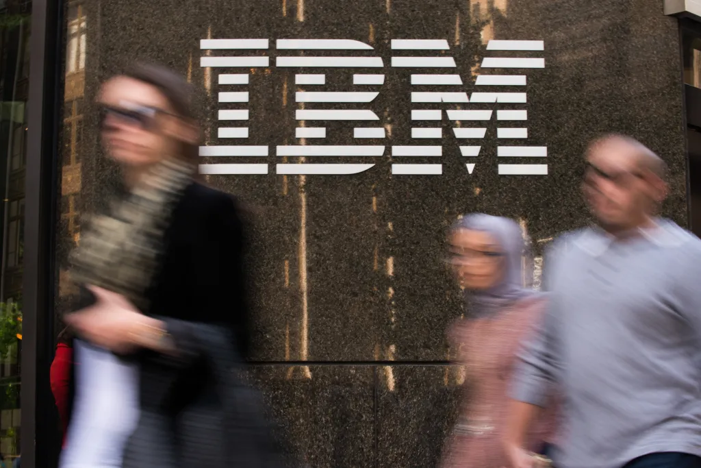 Blurred pedestrians walk past the IBM logo displayed on the company's offices.