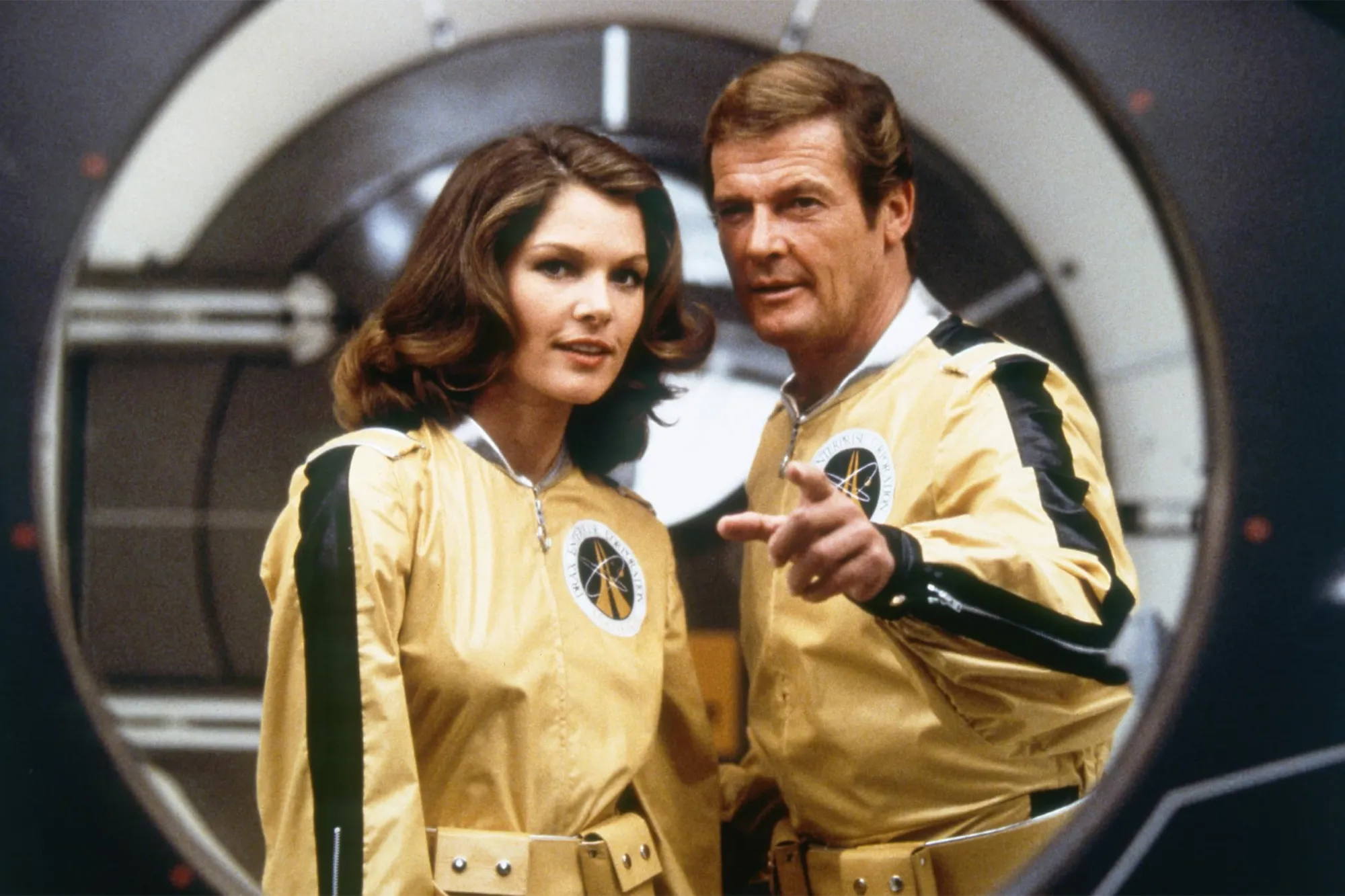 Lois Chiles and Roger Moore as James Bond in Moonraker, wearing gold jumpsuits with 