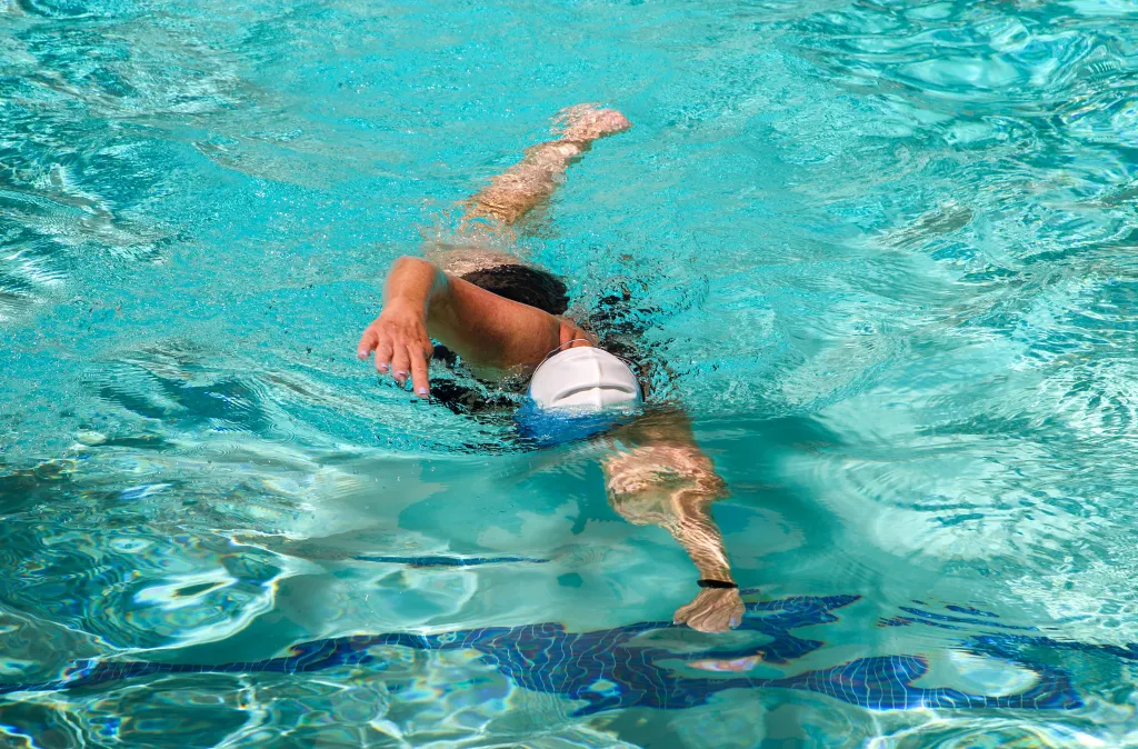 Female swimmer in a hotel pool with a white cap, swimming laps.