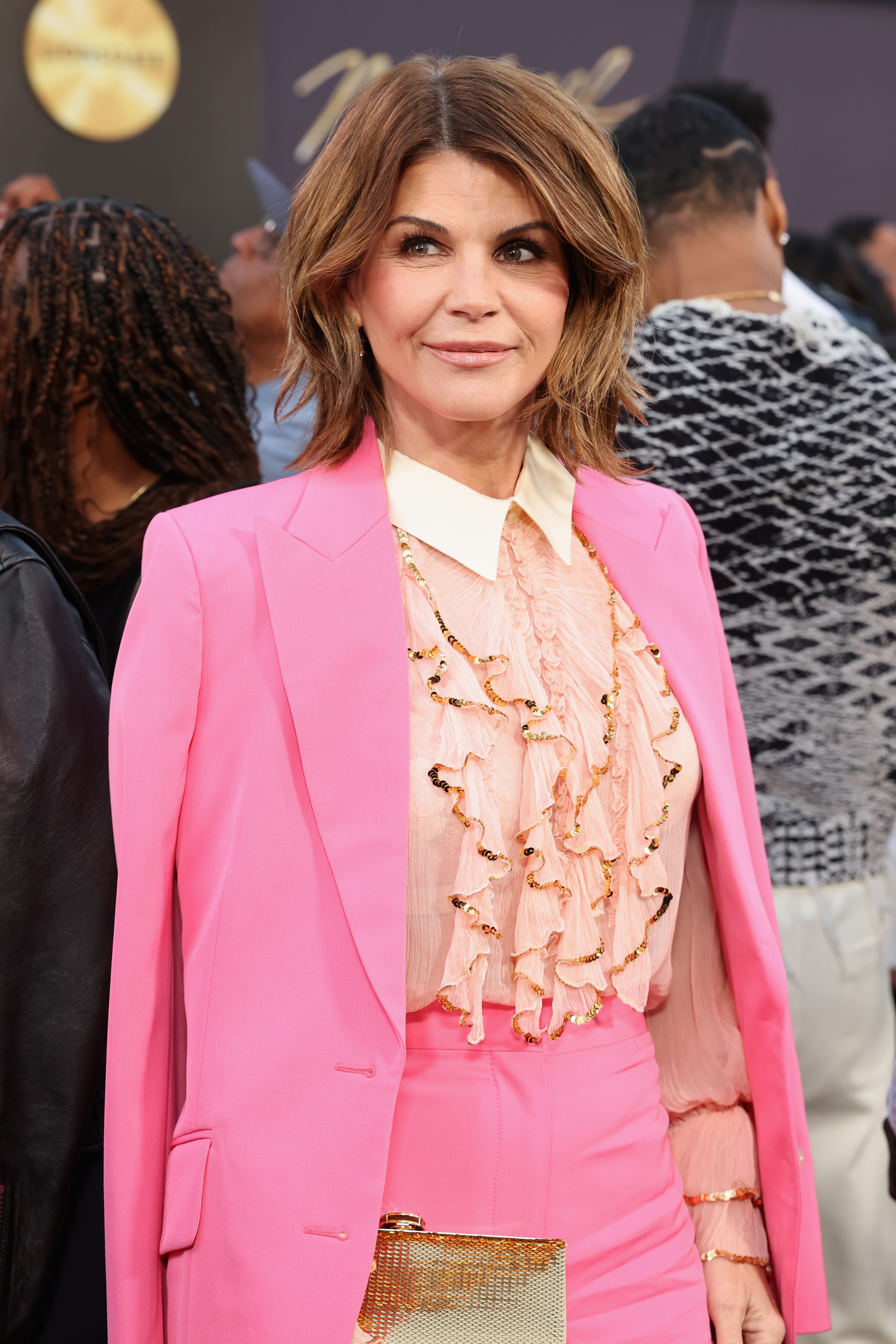 Lori Loughlin in a pink suit with a ruffled blouse.
