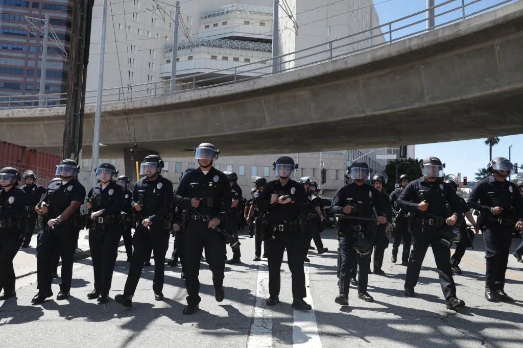 Los Angeles Police Department officers in riot gear marching in a street during an anti-ICE protest.