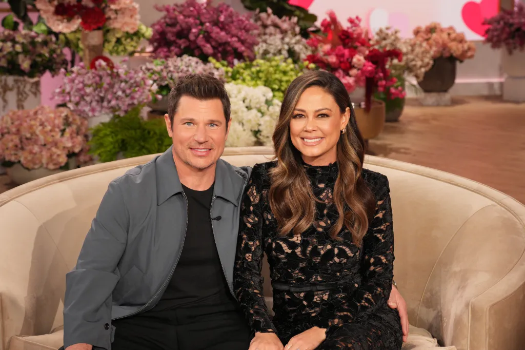 Nick and Vanessa Lachey sitting on a sofa in front of a floral background.