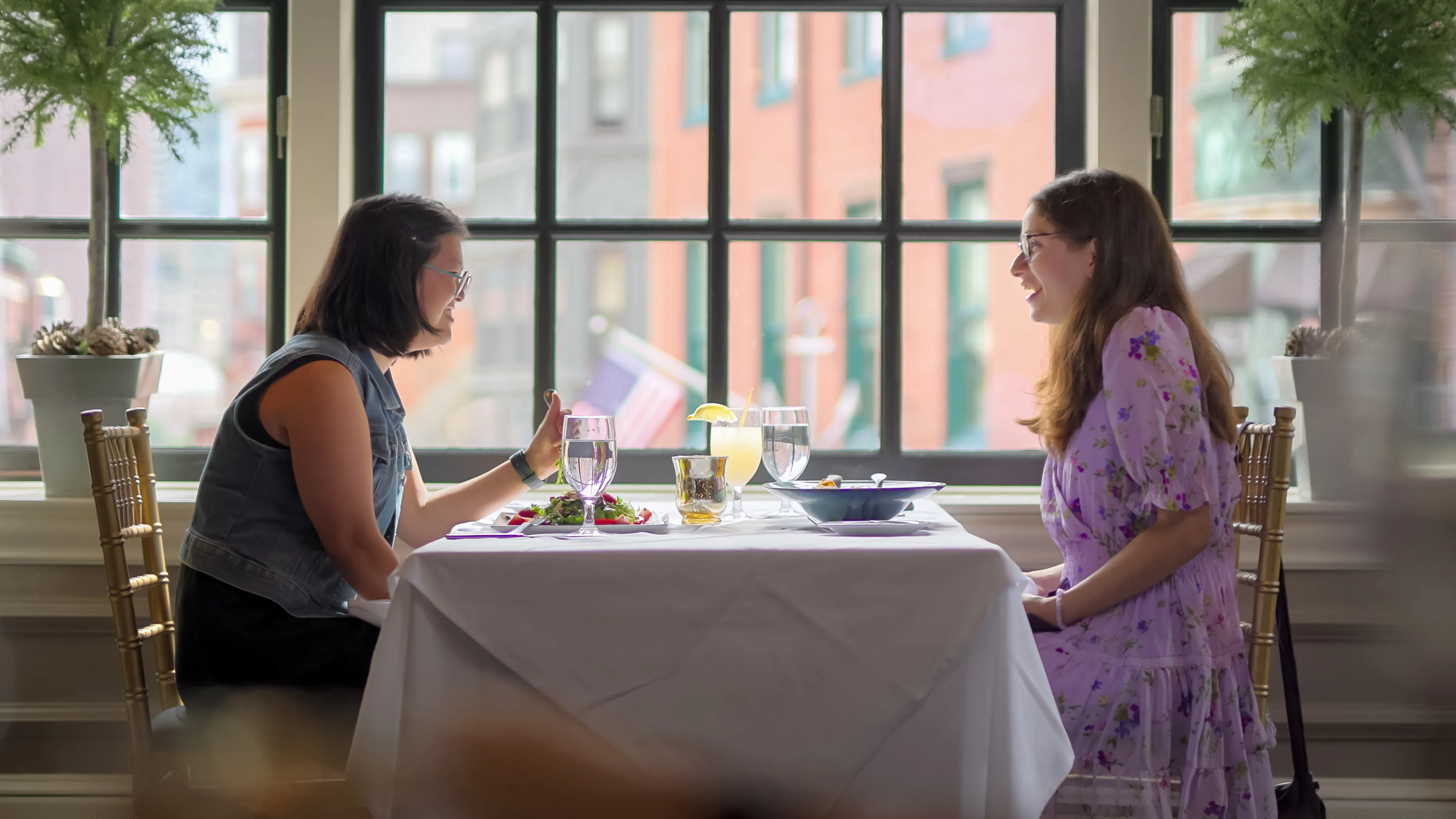 Two women smiling at each other across a table at a restaurant.
