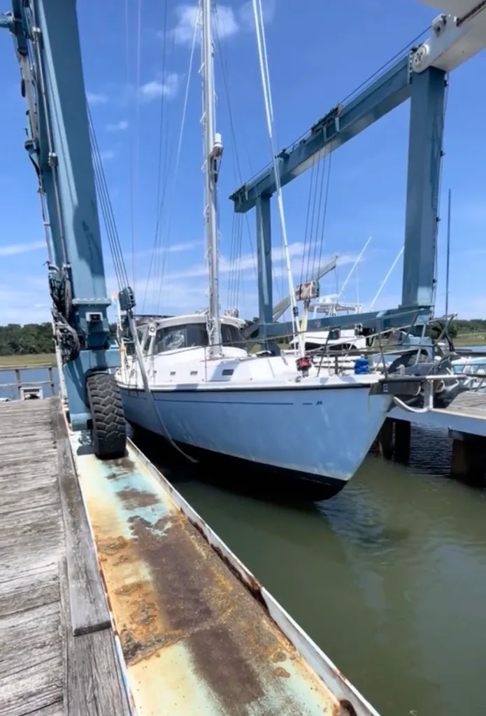 A sailboat being lifted out of the water by a boat hoist.