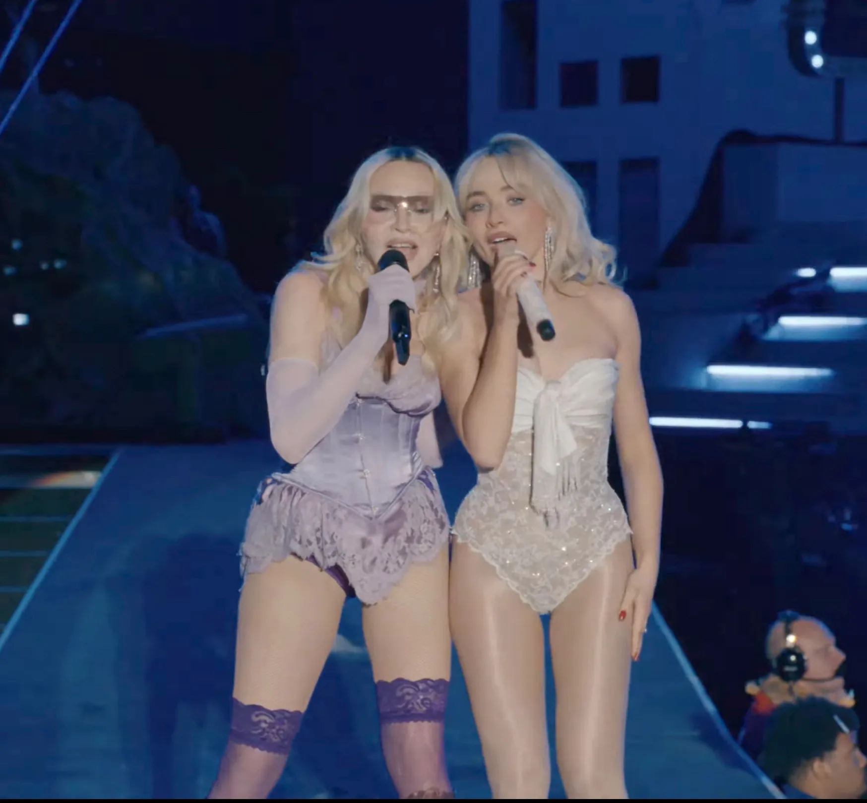 Madonna and Sabrina Carpenter performing together on stage, holding microphones.
