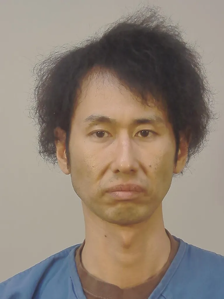 Mugshot of Makoto Kuroda, a man with disheveled dark hair, wearing a brown shirt under a blue top.