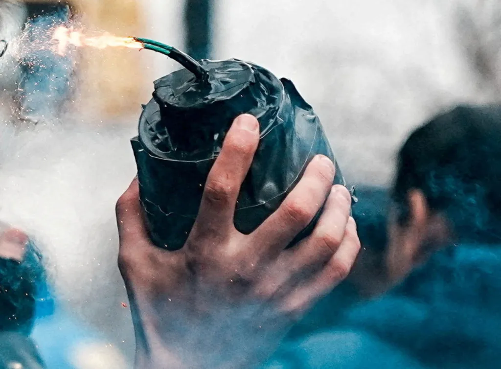 A hand holding an alleged hand-made explosive with a lit fuse.