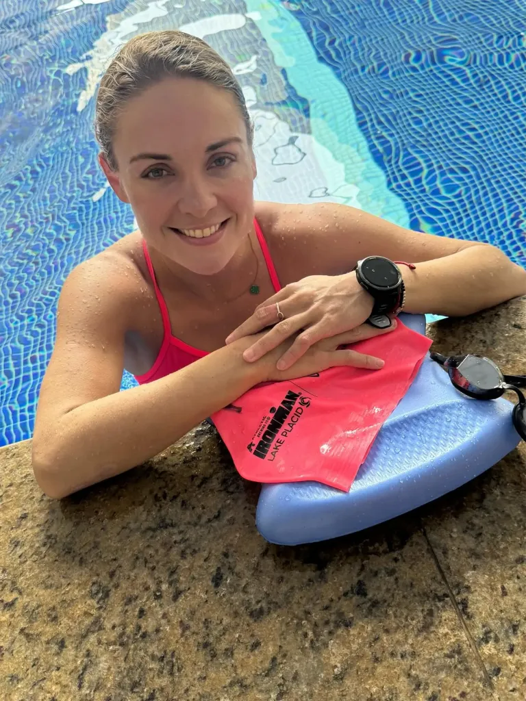 Woman in a pink swimsuit in a pool, holding a kickboard and wearing a smartwatch and goggles.