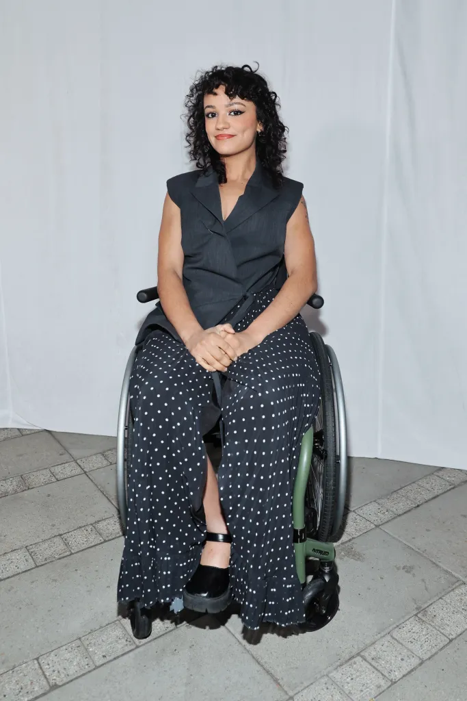 Marissa Bode in a wheelchair wearing a charcoal sleeveless jacket and a black polka-dot maxi skirt.