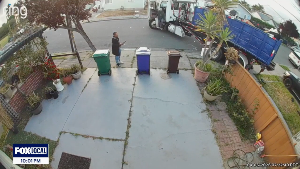 A man standing on a driveway while a dumpster truck dumps its contents onto the property.