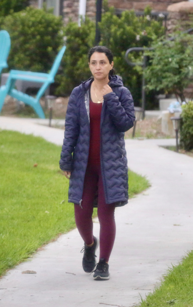 Maryam Tahmasebi, detained by ICE and slated for deportation, walks outdoors in a dark blue puffer jacket over a red shirt and maroon leggings.