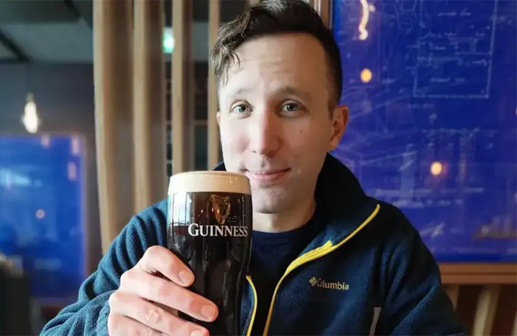 A man in a blue fleece jacket holding a glass of Guinness.