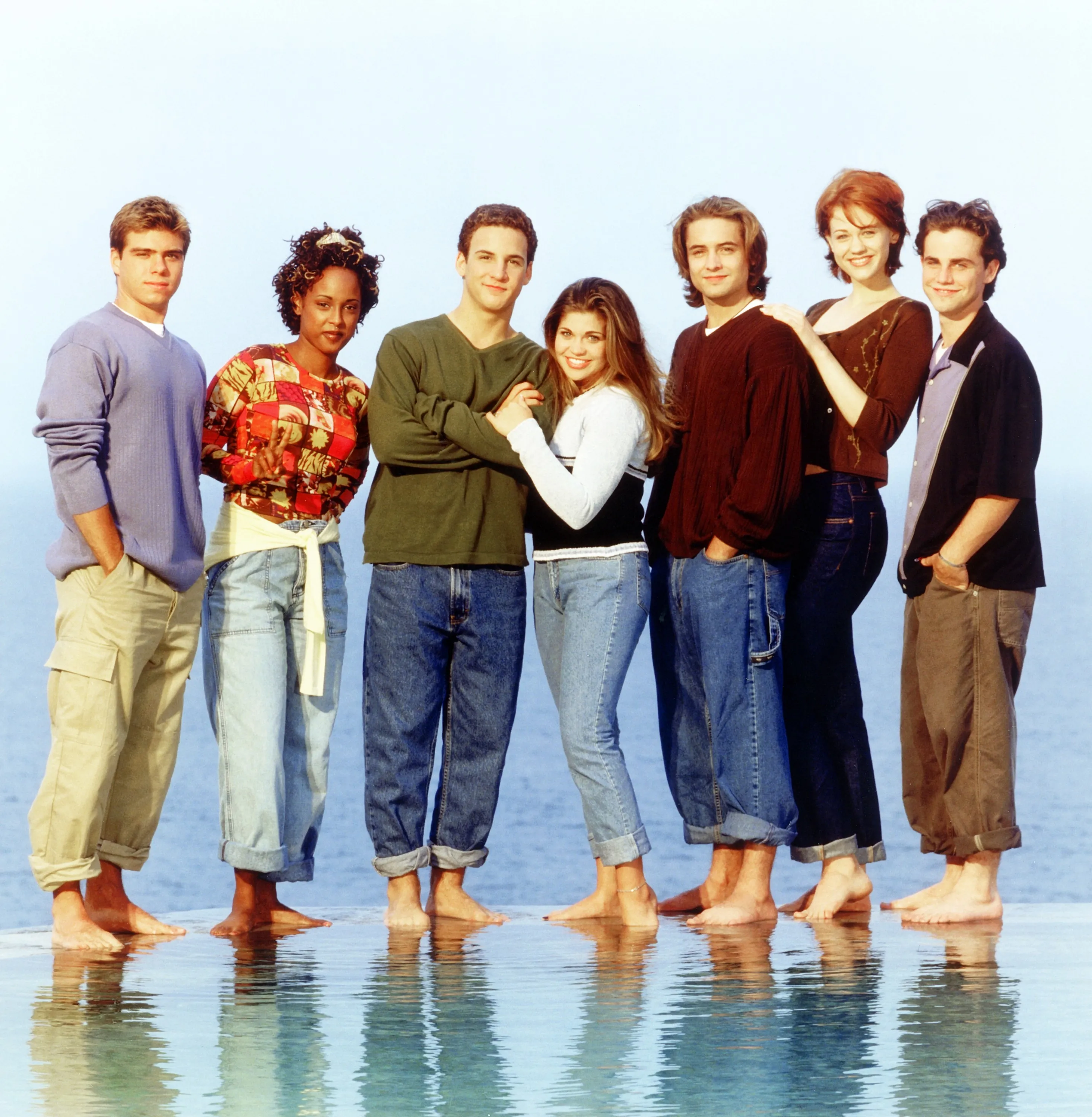 Cast of Boy Meets World: Matthew Lawrence, Trina McGee, Ben Savage, Danielle Fishel, Will Friedle, Maitland Ward, and Rider Strong standing barefoot by water.