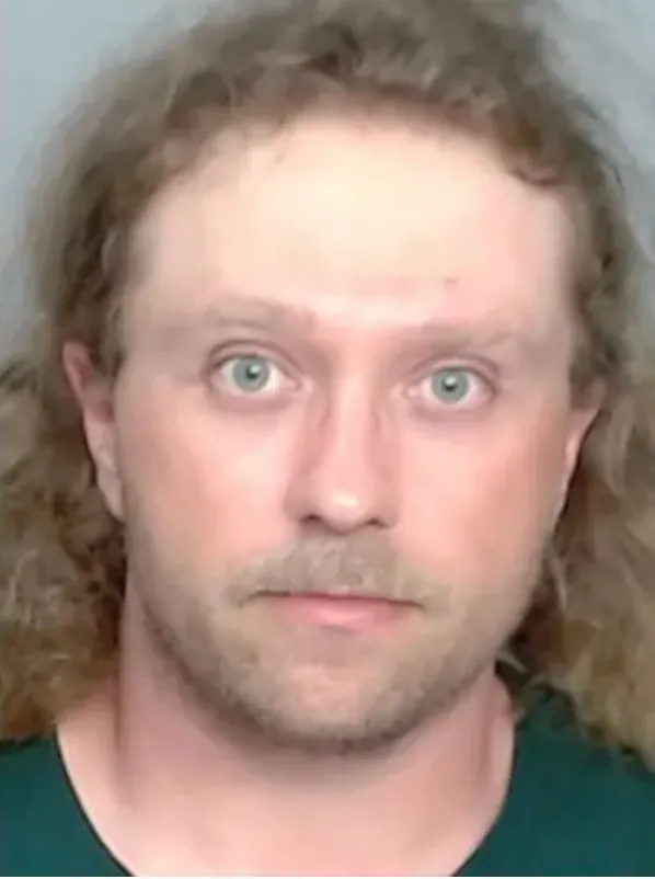 Mugshot of a man with long, curly blonde hair and a mustache.