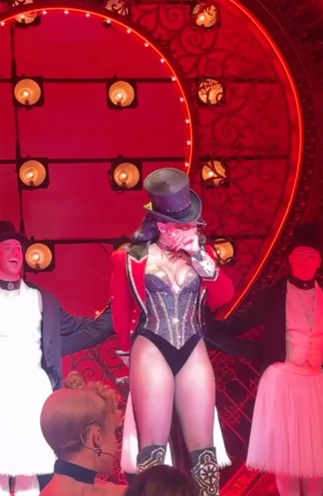 Megan Thee Stallion in a top hat and a sparkly corset with a red jacket, crying on stage during a Broadway performance.