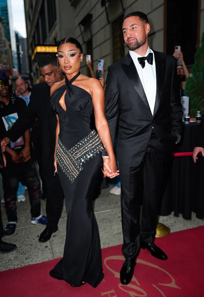 Megan Thee Stallion in a black gown and Klay Thompson in a black tuxedo walking hand-in-hand.