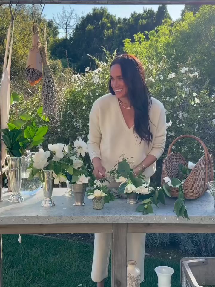 Meghan Markle arranging flowers on a table outdoors.