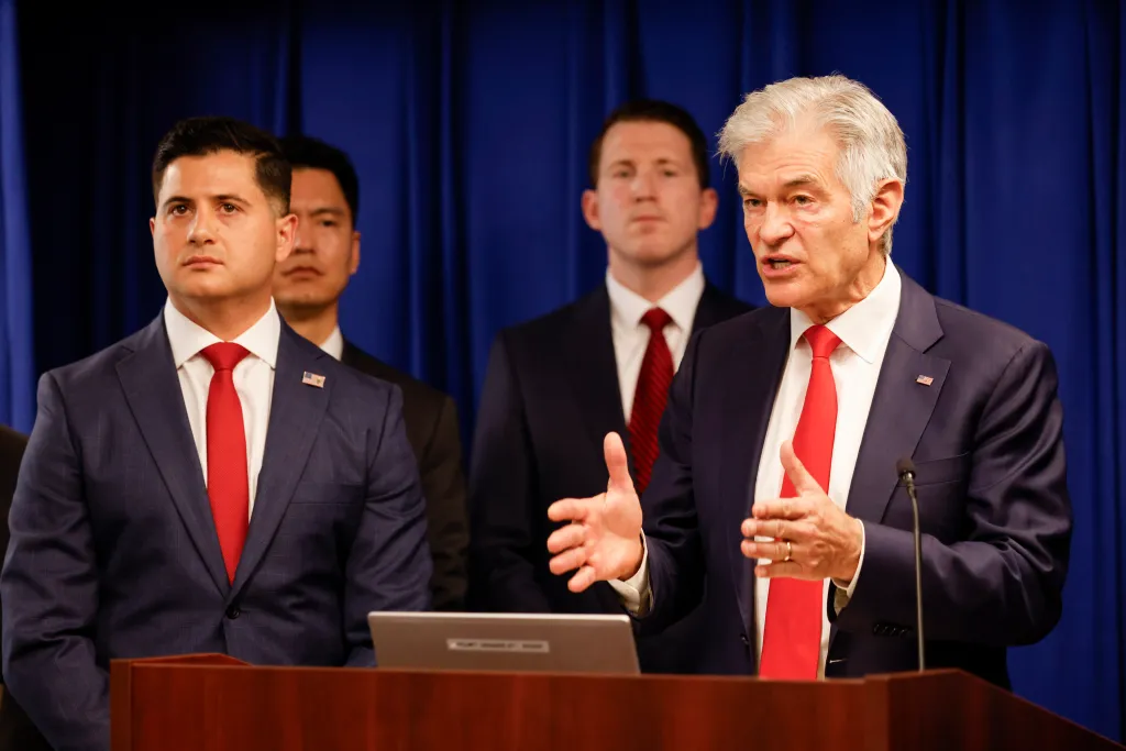 Mehmet Oz speaking about the fraud epidemic at a press conference with other men in suits in Los Angeles.