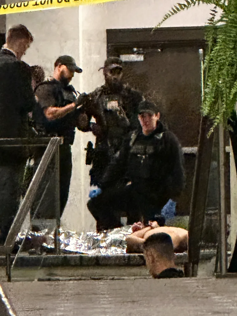Law enforcement personnel respond to an incident, with one person lying on the ground covered in foil.