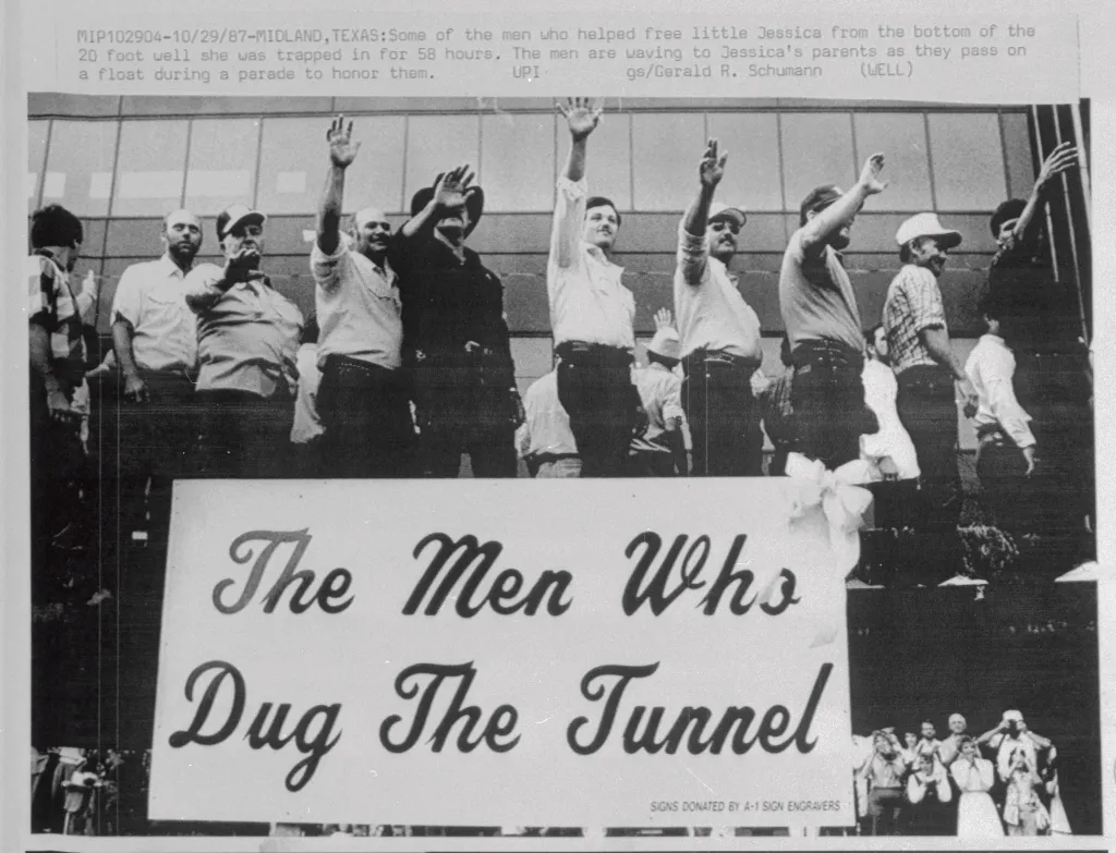 Men who rescued Jessica McClure wave during a parade, behind a banner that reads