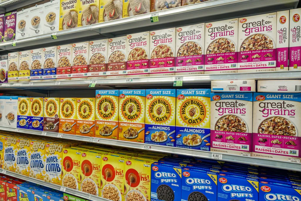 A supermarket aisle with shelves full of Post brand cereals, including Great Grains, Honey Bunches of Oats, Honeycomb, and Oreo O's.