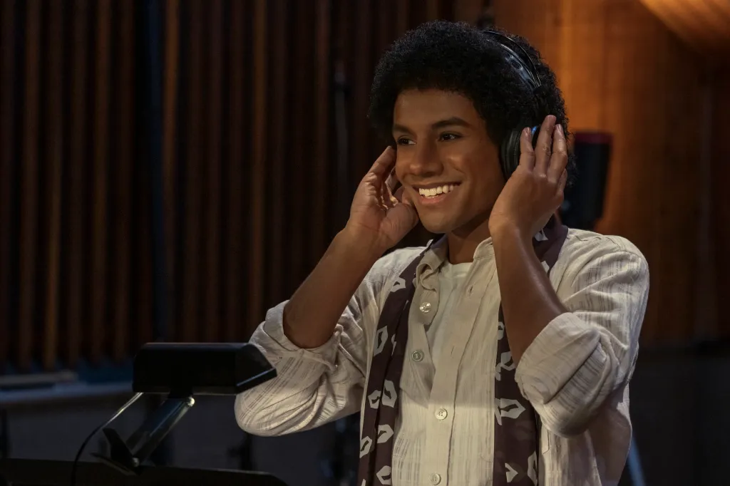 Jaafar Jackson as Michael Jackson smiling while wearing headphones in a recording studio.