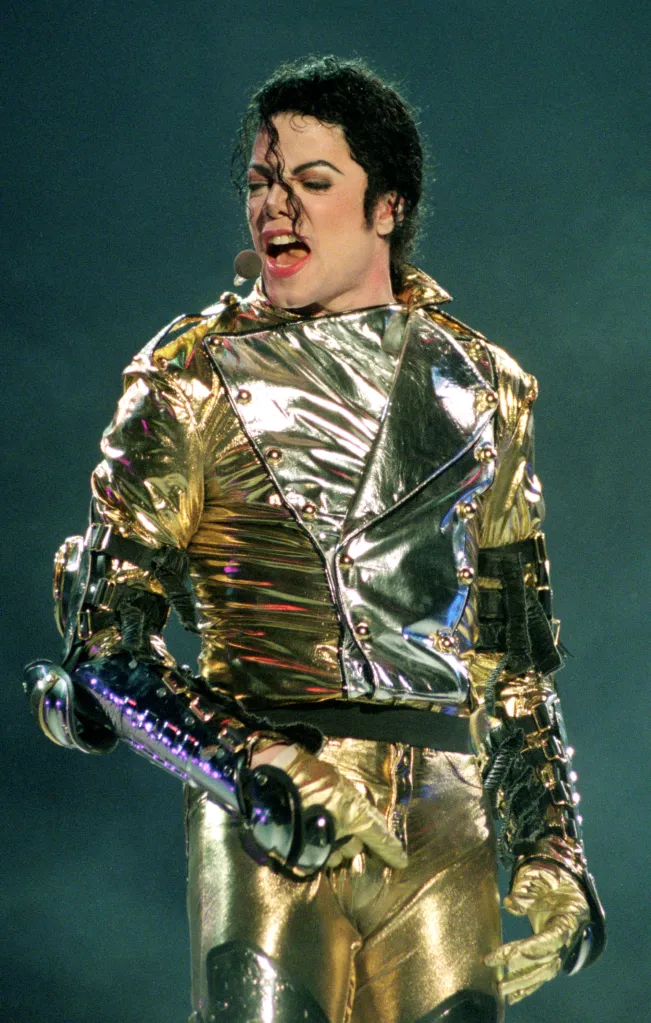 Michael Jackson singing on stage, wearing a shiny gold and silver outfit and gold gloves.