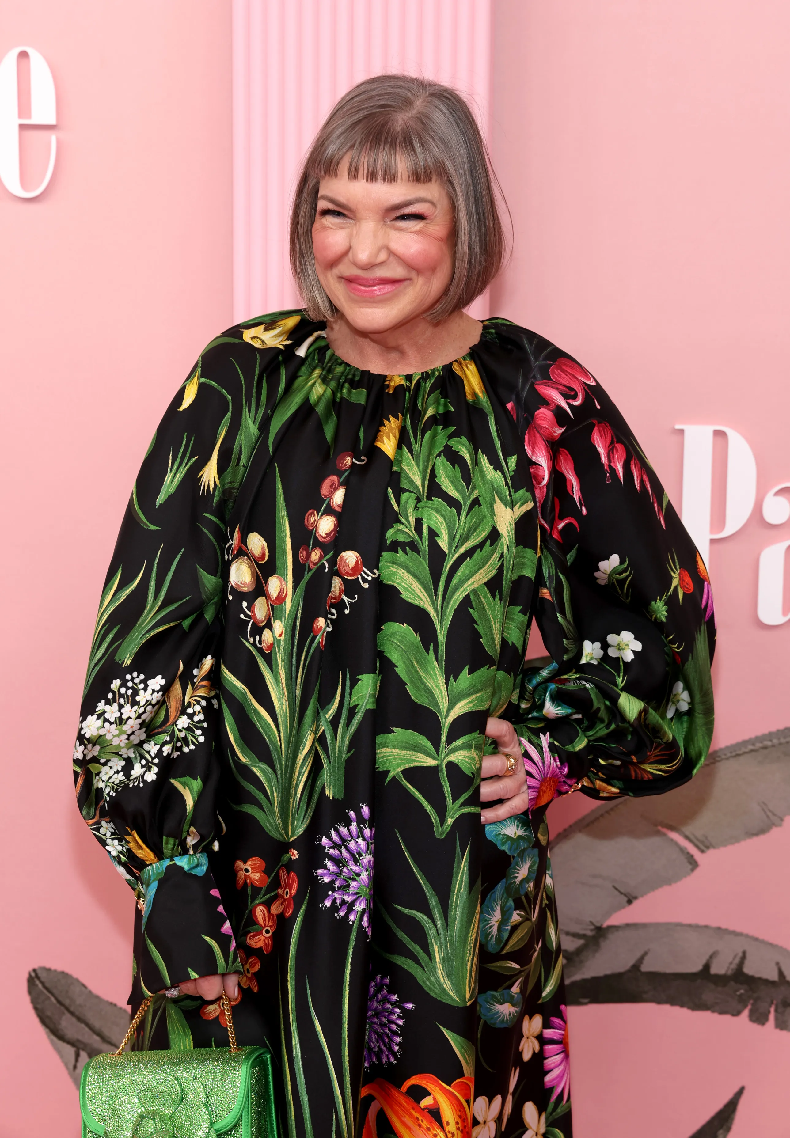 Mindy Cohn smiles at the camera, wearing a flowing black dress with a vibrant floral pattern.
