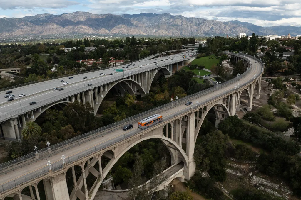 Aerial view of motorists on the historic Colorado Street Bridge and a freeway in Pasadena, California, with mountains in the background.