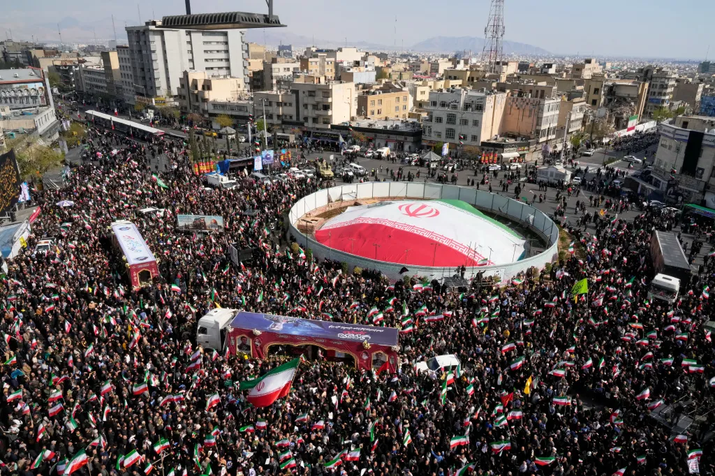 Mourners, many holding Iranian flags, fill a city street during a funeral procession for Alireza Tangsiri and others.