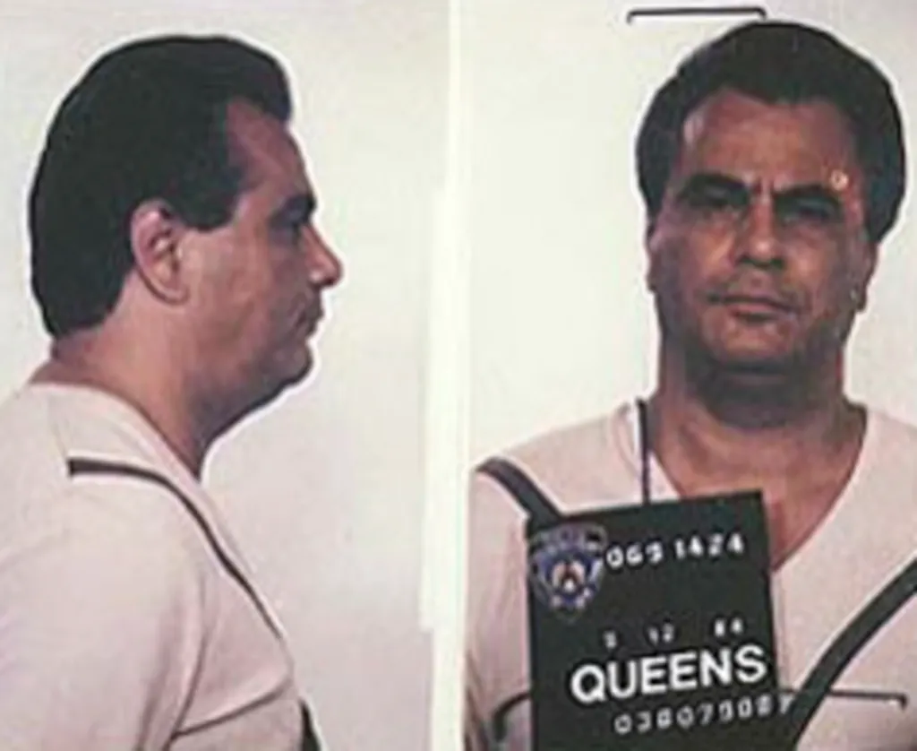 Mug shot of John Gotti, with a profile view on the left and a front-facing view on the right, holding a sign that says 