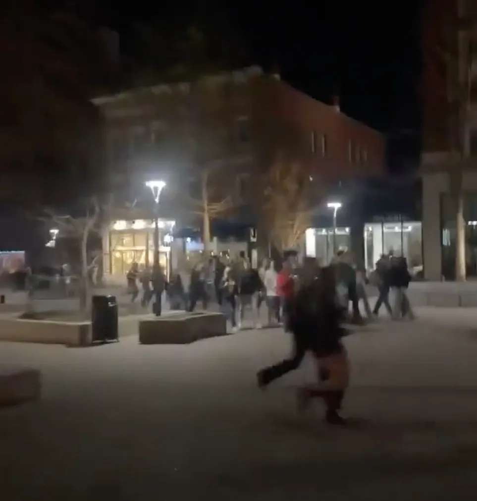 People running from gunshots in an outdoor mall at night.