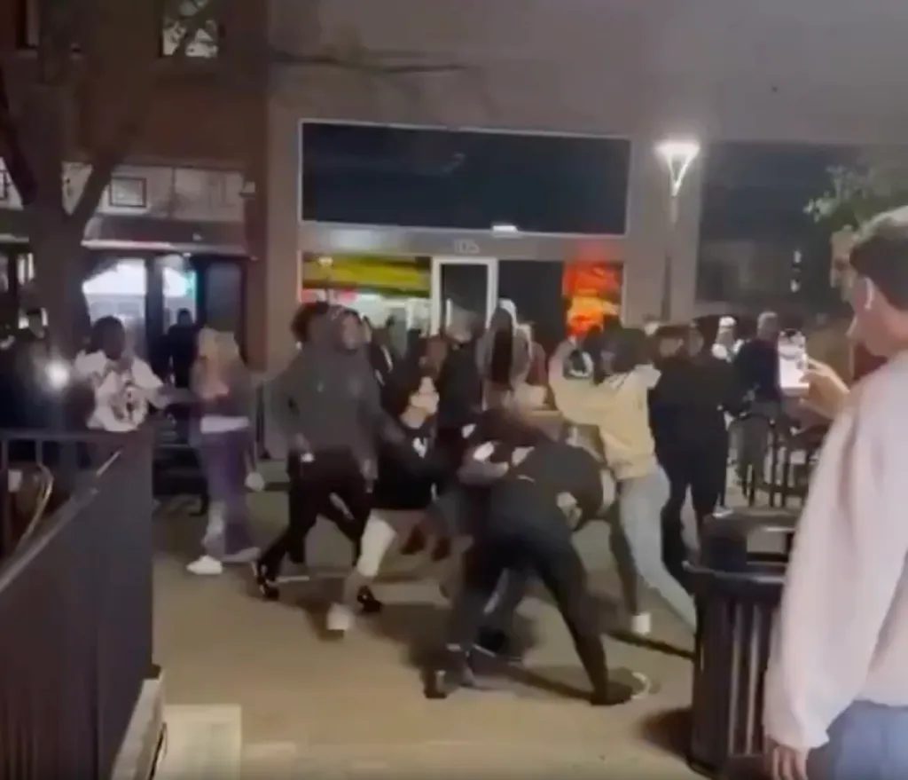 Multiple people involved in a brawl on a street at night.