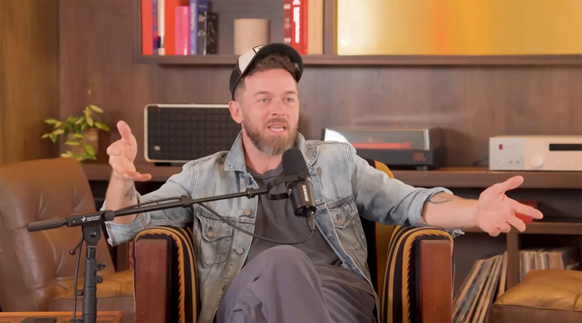 Artem Chigvintsev with a beard and baseball cap gestures with both hands while speaking into a microphone.