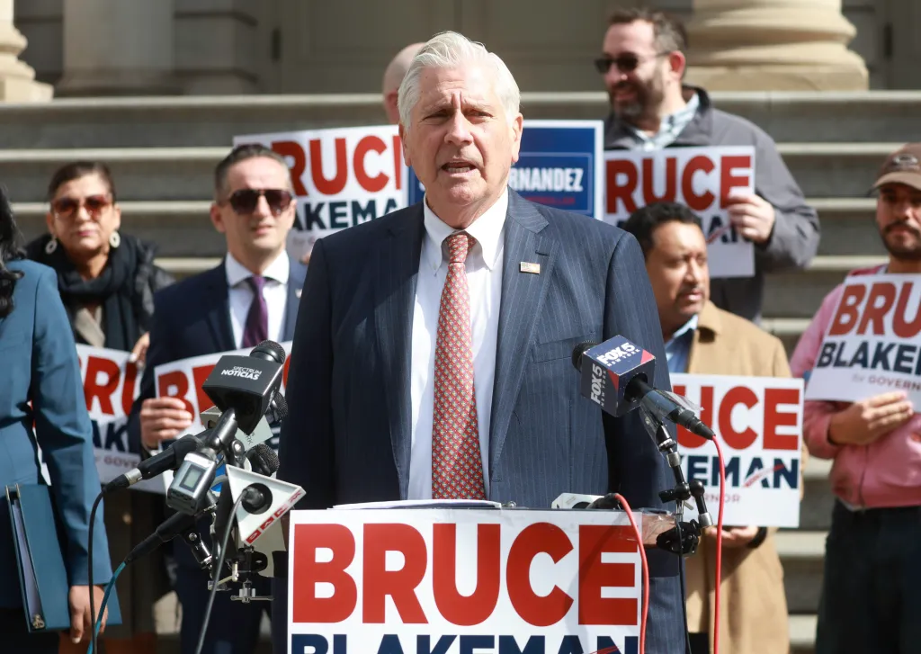 Nassau County Executive Bruce Blakeman speaks at a press conference in front of NYC City Hall, flanked by supporters holding 