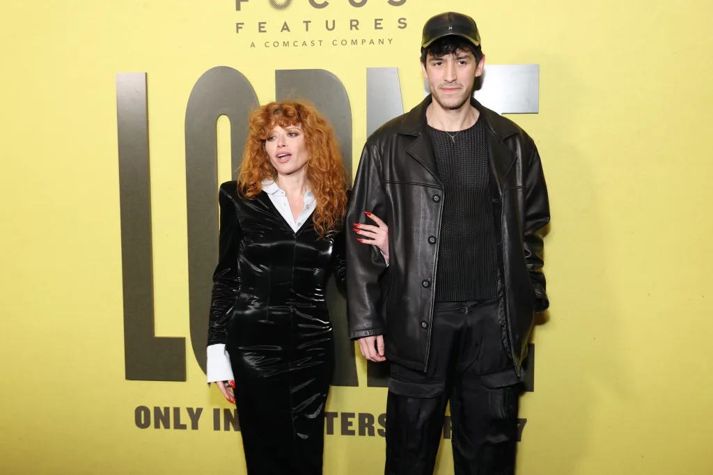 Natasha Lyonne, in a black coat and white shirt, with Hamer Morgenstern, in a black leather jacket, black t-shirt, black pants and black baseball cap.