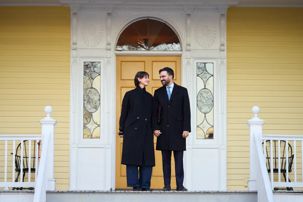 New York City Mayor Zohran Mamdani and his wife, First Lady Rama Duwaji, holding hands in front of Gracie Mansion.