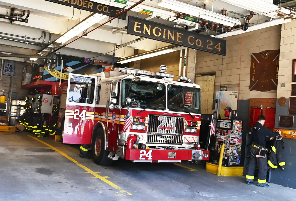 FDNY Engine 24 truck parked inside a firehouse, with a firefighter in uniform standing next to the truck.
