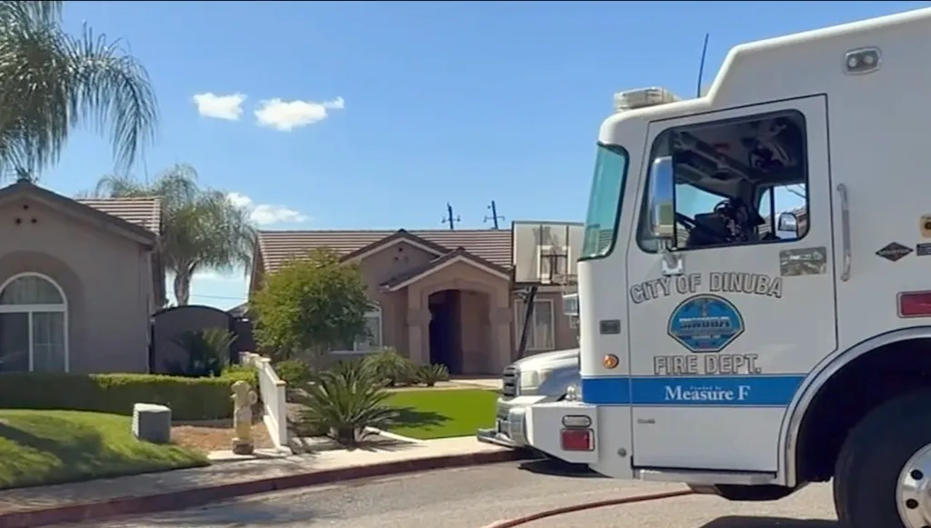 A Dinuba Fire Department truck parked in front of houses with green lawns and palm trees.