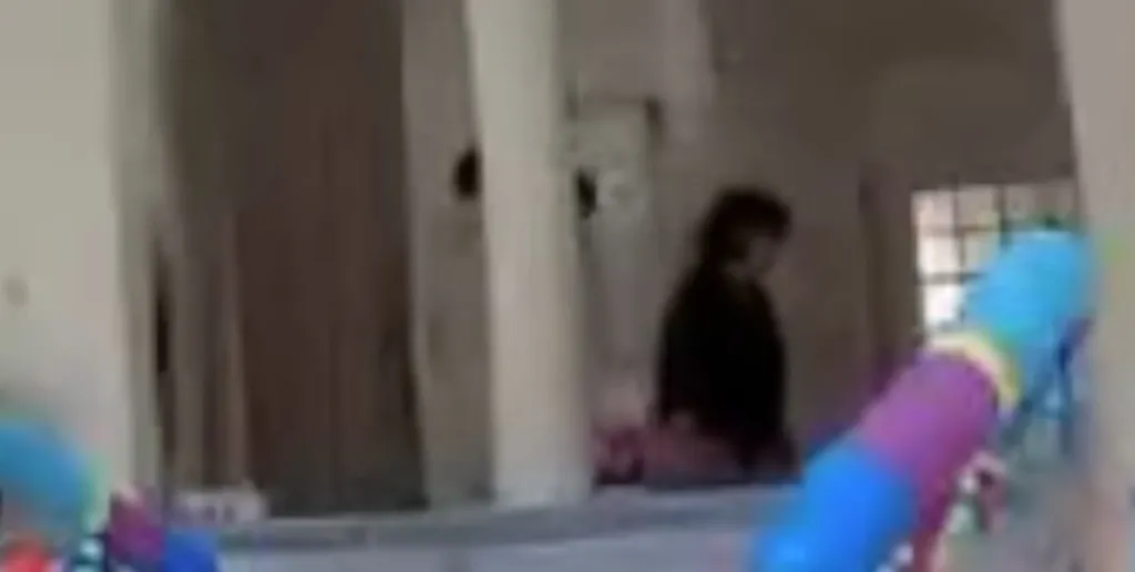 Blurry image showing a woman with dark hair in a dark top standing in a doorway.