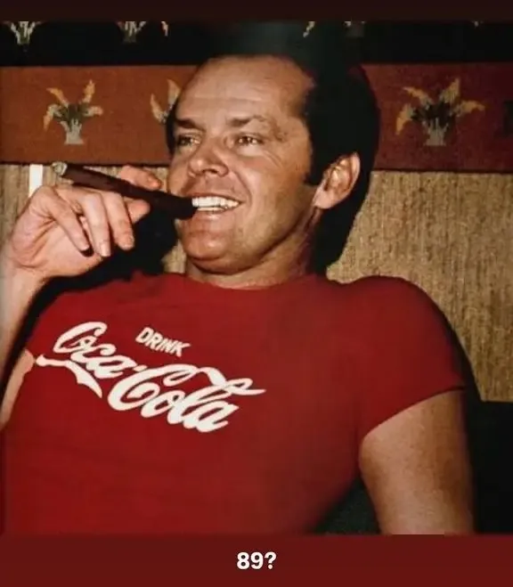Jack Nicholson in a red Coca-Cola shirt, smiling with a cigar in his mouth.