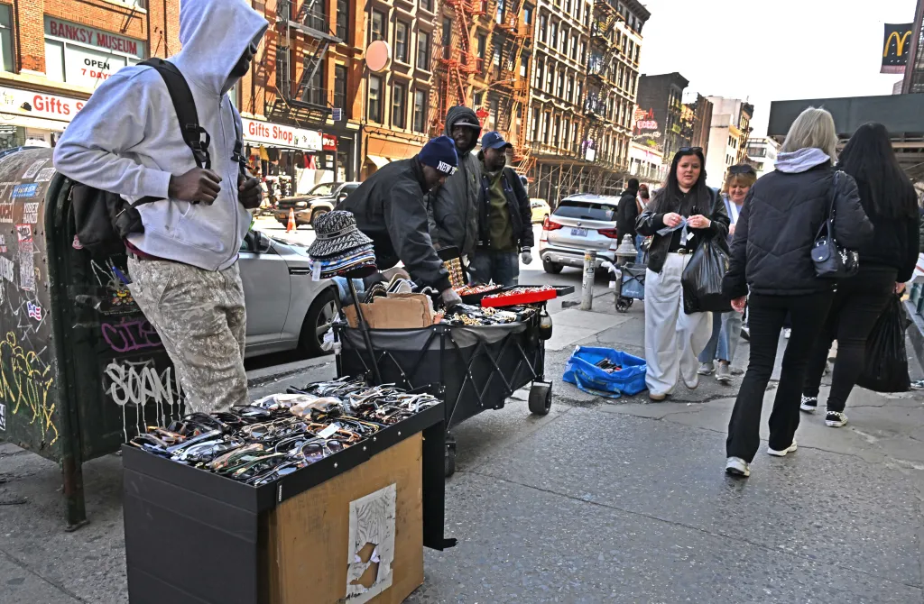 Men selling hats and sunglasses from carts on a street in New York City.