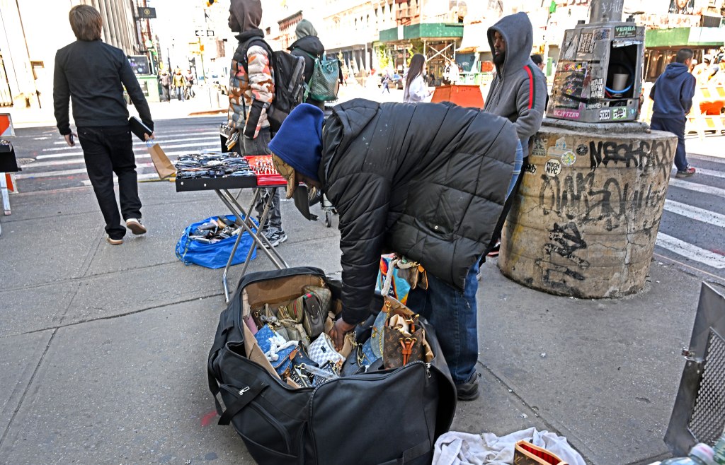 Vendor on Canal Street sorting through bags and wallets in a large duffel bag on the sidewalk.