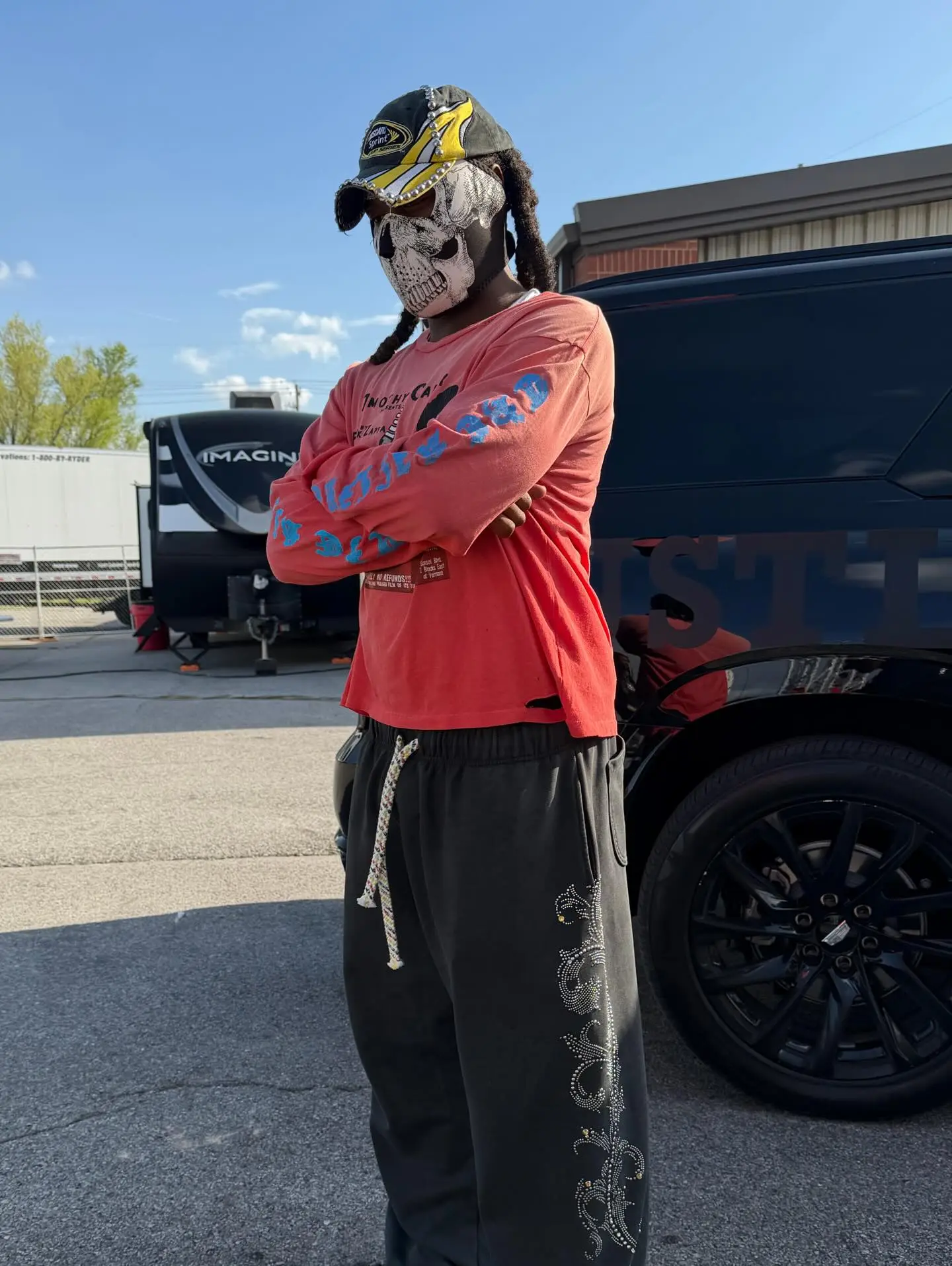 Offset wearing a skull mask, a baseball cap, a salmon long-sleeve shirt, and dark pants with white embroidered designs.