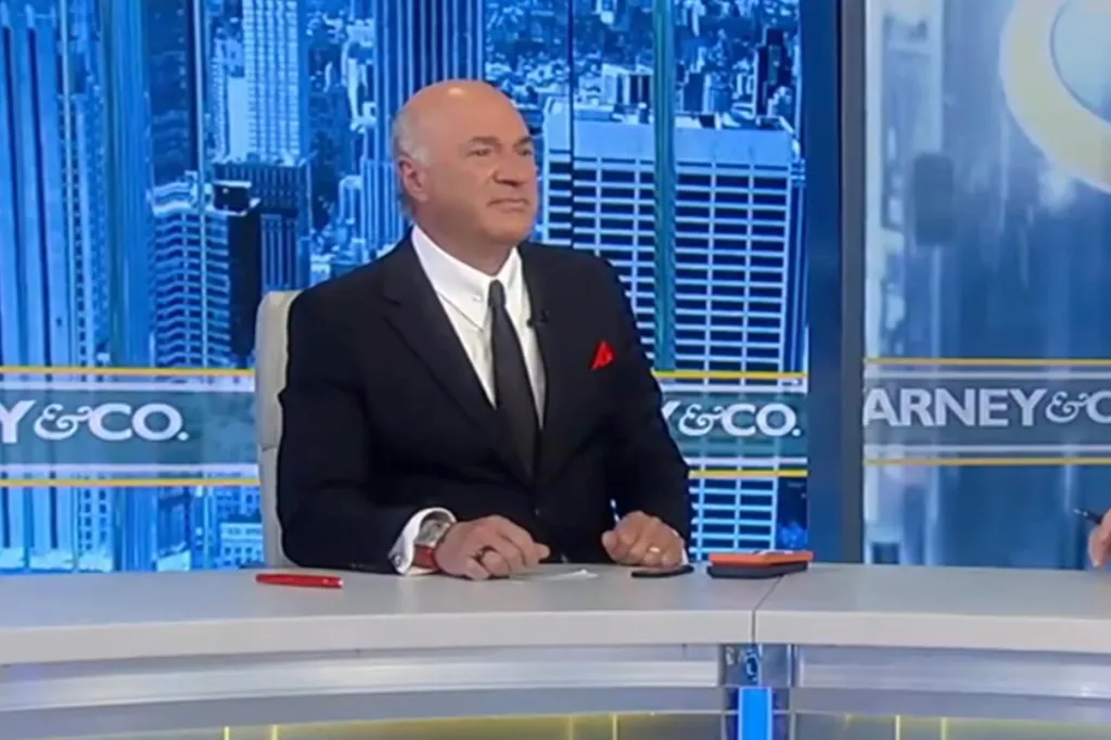 Kevin O'Leary at a desk with a city skyline backdrop.